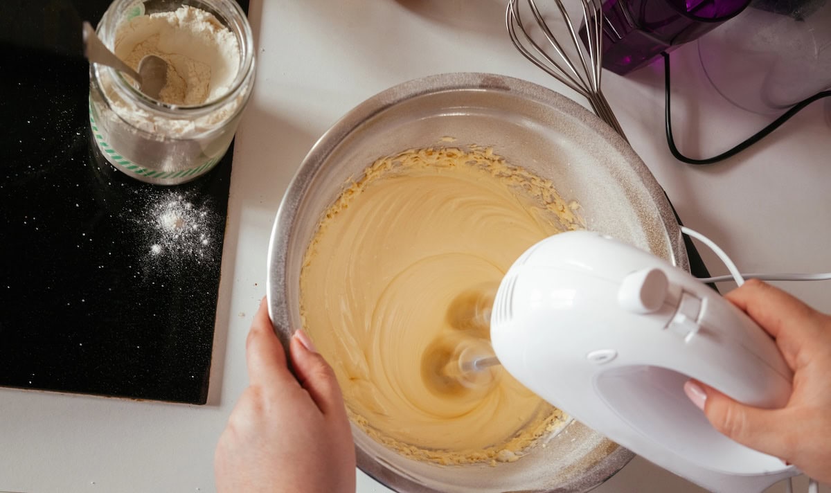 Mixing batter for yellow cupcakes in a stainless bowl with a mixer.