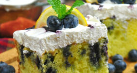 Lemon Poke Cake with blueberries on a wood cutting board with blueberries.