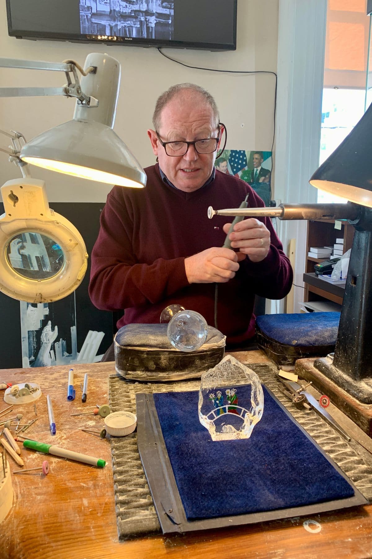Man sitting at desk with etching tool and a glass in front of him along with other tools.