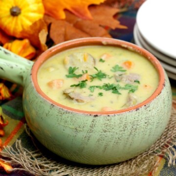 Cheddar cheese soup with bratwurst, carrots and parsley in a light green bowl with a handle