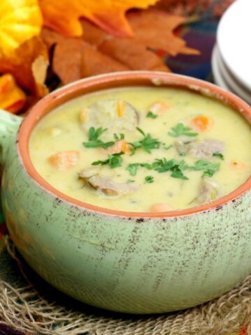 Cheddar cheese soup with bratwurst, carrots and parsley in a light green bowl with a handle