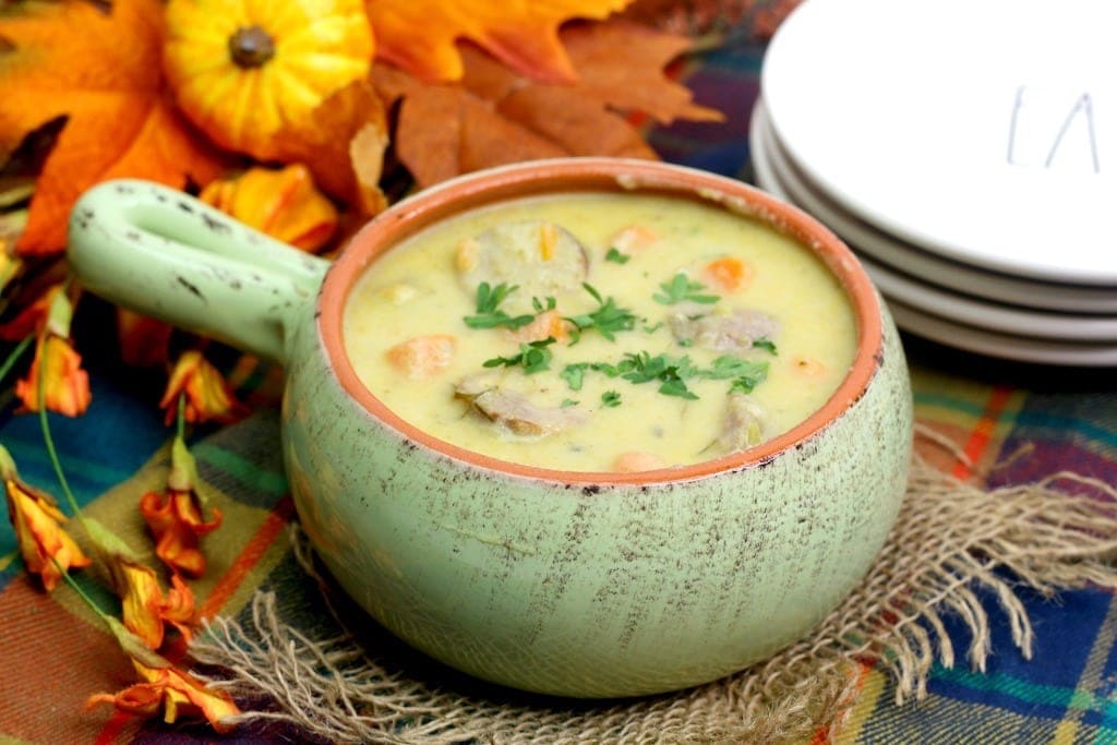 Cheddar cheese soup with bratwurst, carrots and parsley in a light green bowl with a handle