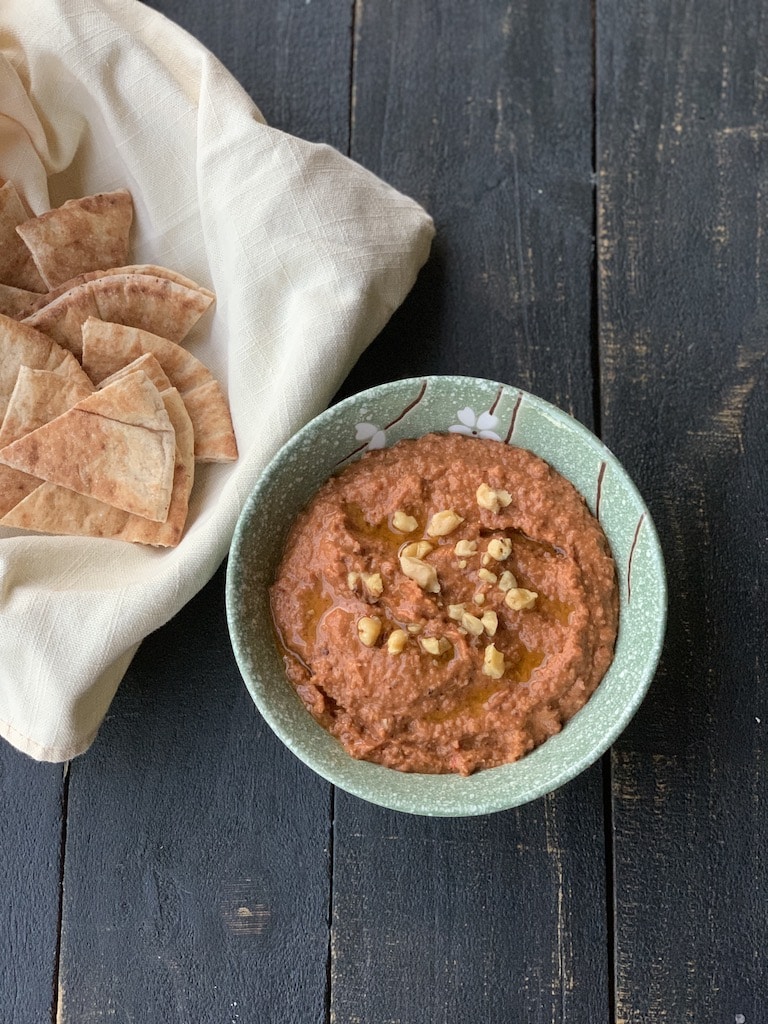 Red pepper dip on black table with pita bread in basket.