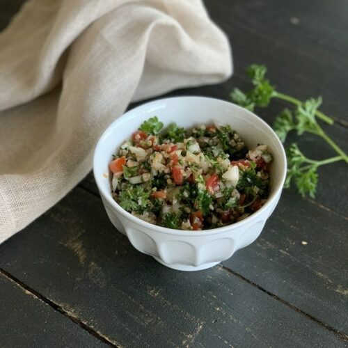 tabbouleh in white bowl on black table with napkin