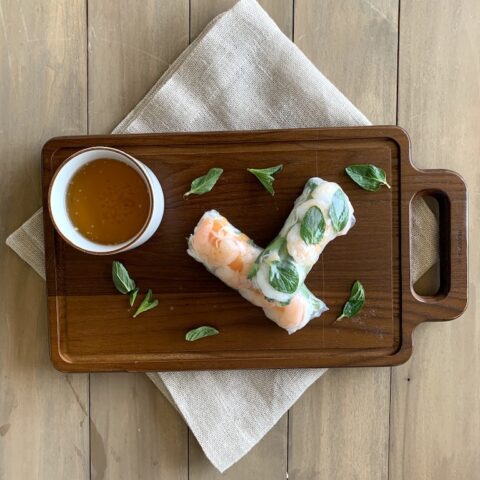shrimp summer rolls on a cutting board over napkin with sauce on side