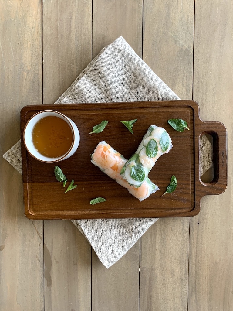 shrimp summer rolls on a cutting board over napkin with sauce on side