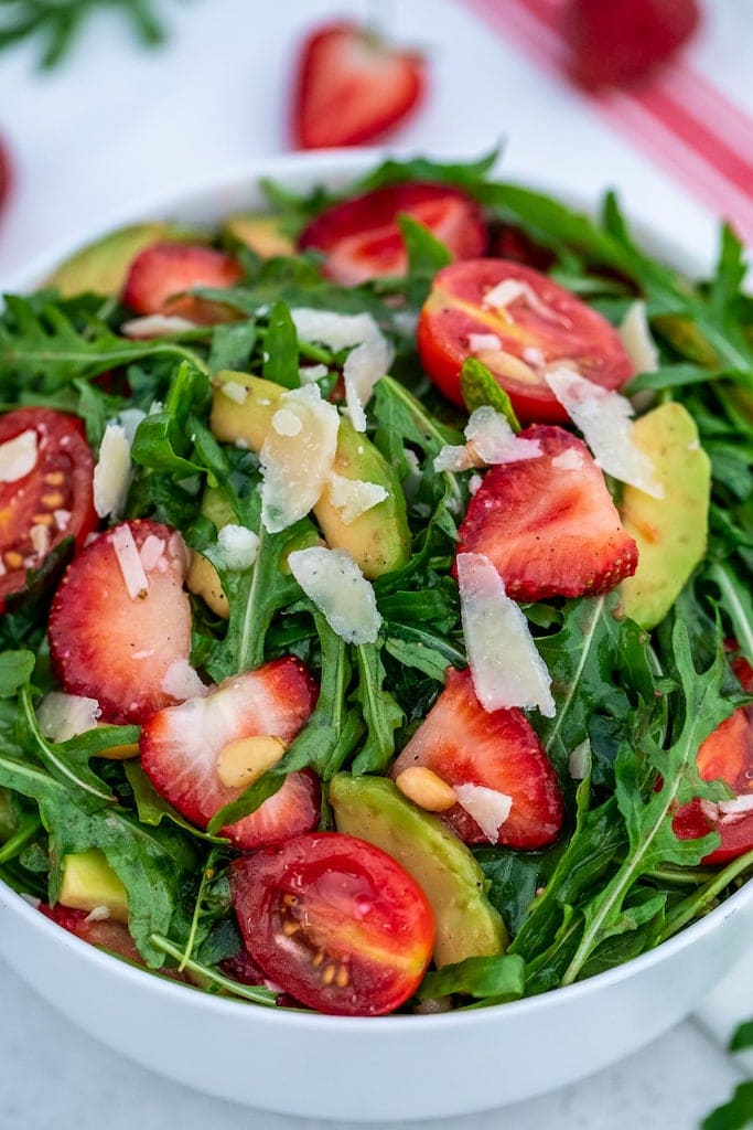 Arugula salad with strawberries  in a white bowl.