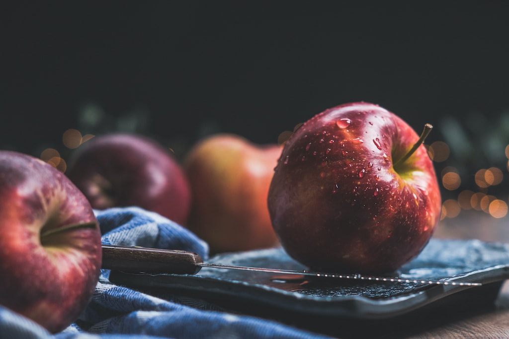 Red apples with one on a blue plate with knife.