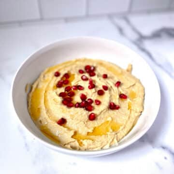 Hummus with olive oil and pomegranate seeds in white bowl.