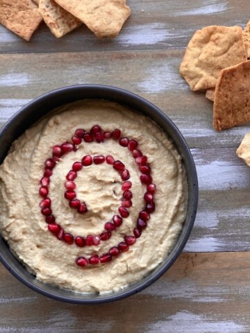 vegan hummus with pomegranate seeds and chips on wood board