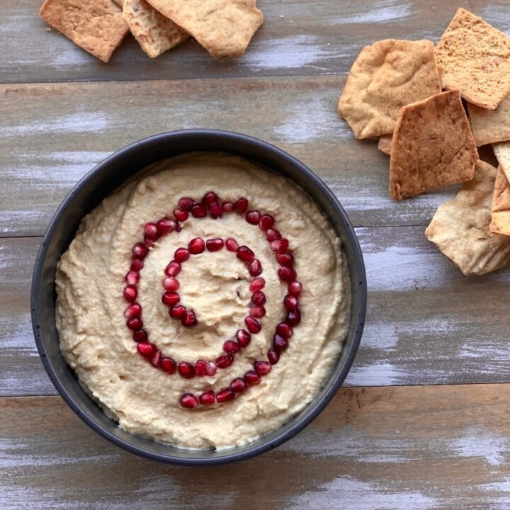 vegan hummus with pomegranate seeds and chips on wood board