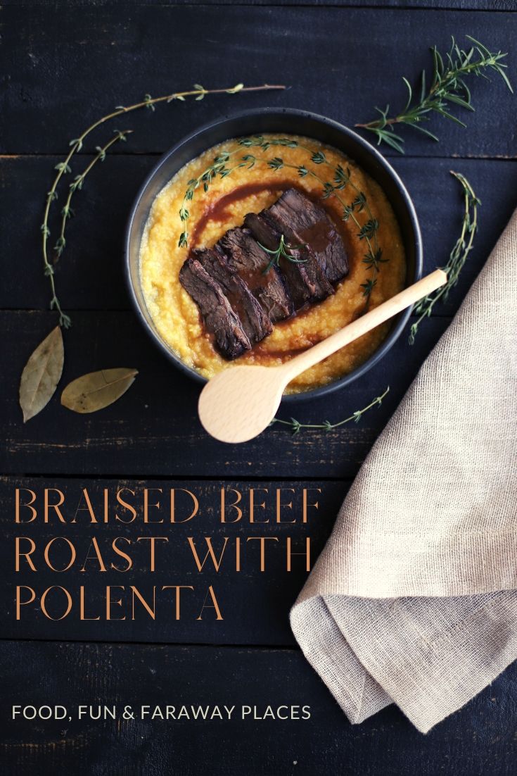 Braised beef over polenta with rosemary, thyme, and juices in a black bowl on a black board for Pinterest