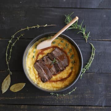 Sliced beef over polenta with gravy and herbs.
