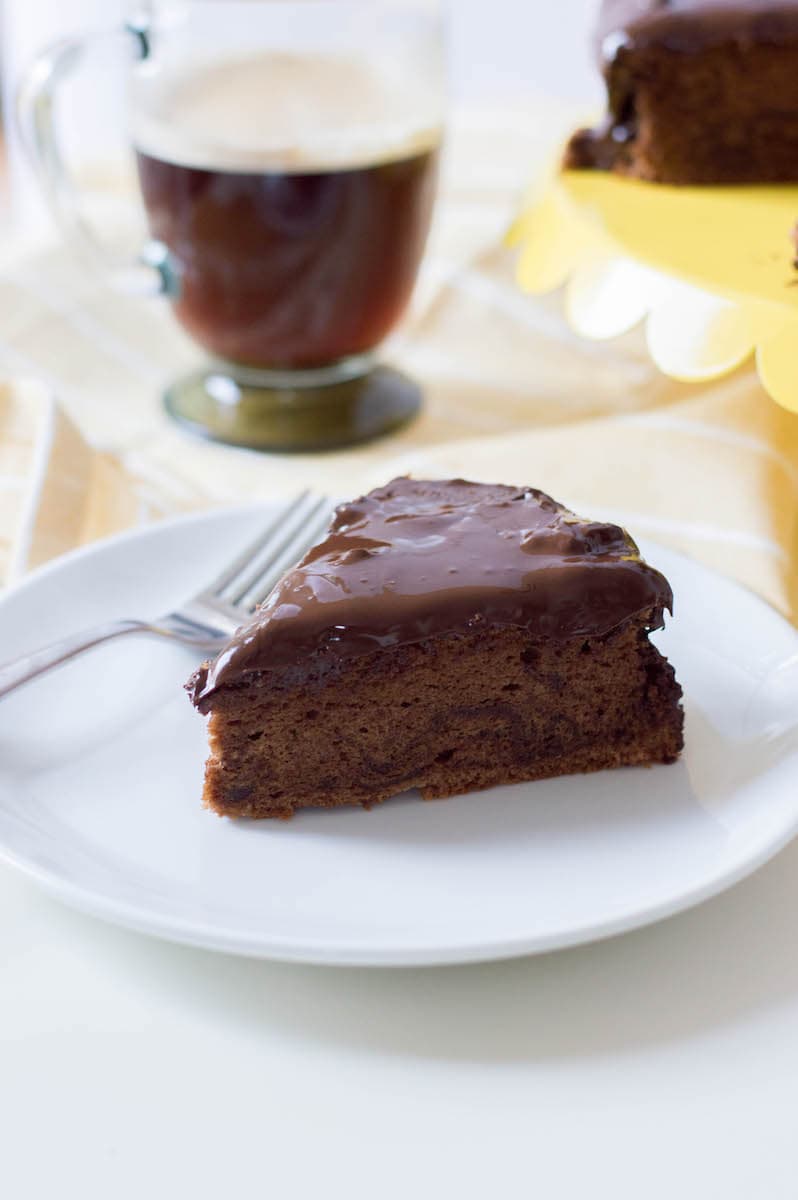 chocolate cake with chocolate icing on white plate with black coffee in background