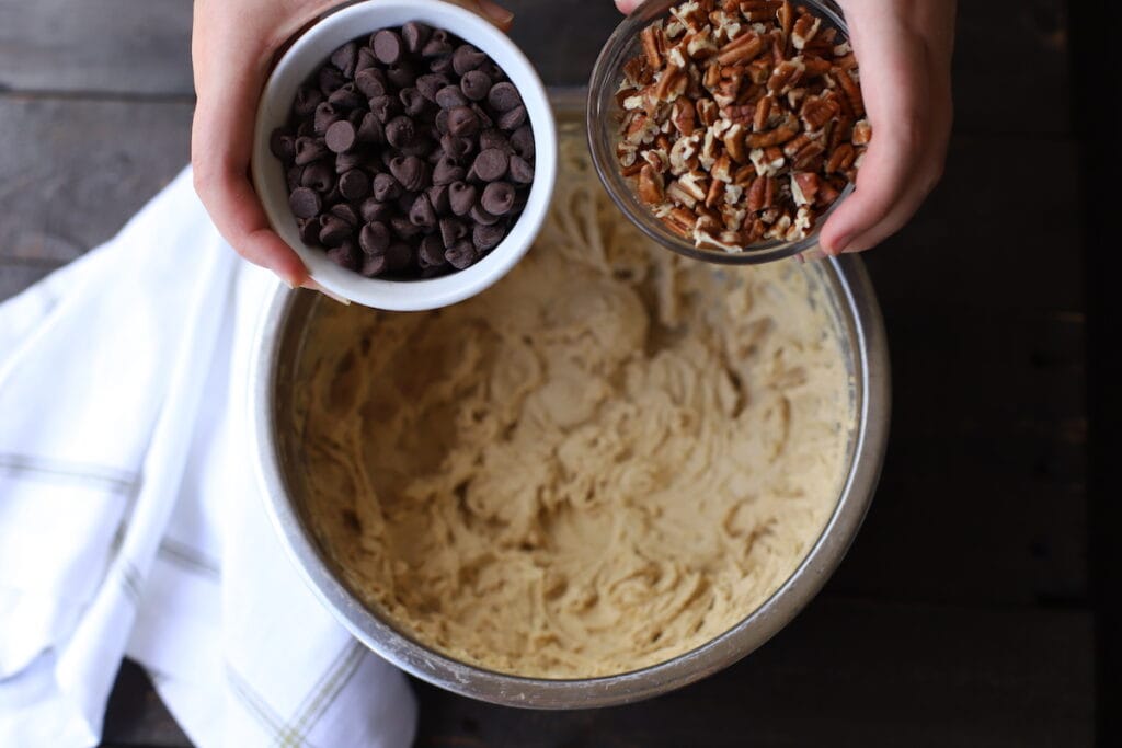 bowl of chocolate chips and bowl of pecans over bowl of batter