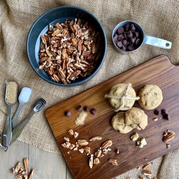 chocolate chip cookies on wood board with pecans, chocolate chips, and spices
