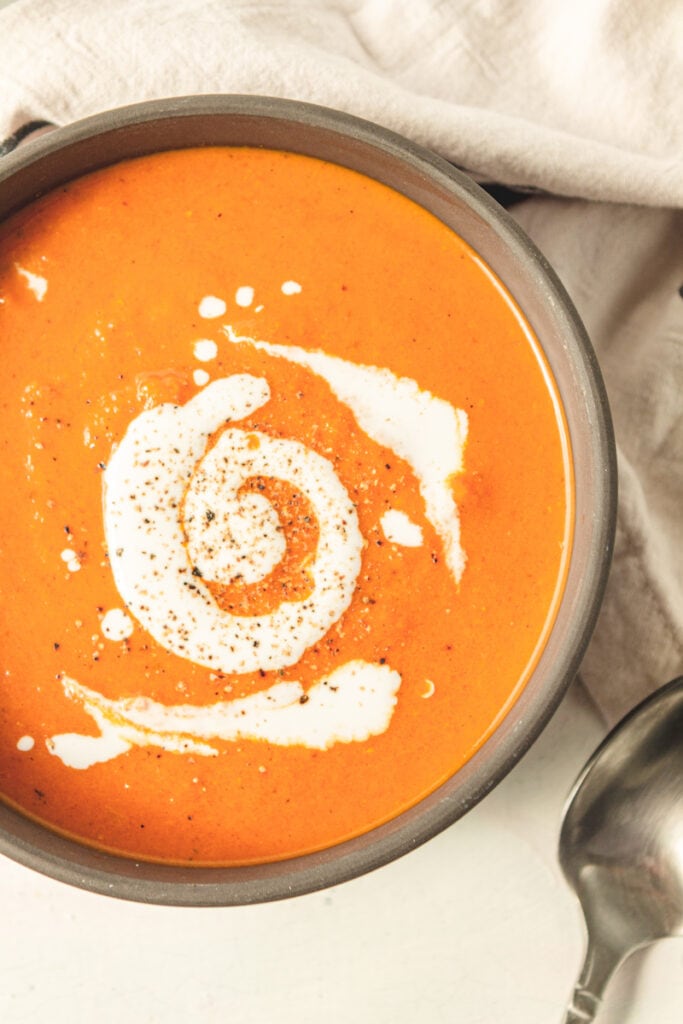 homemade tomato soup recipe with a swirl of coconut  milk on top in a brown bowl on a white table