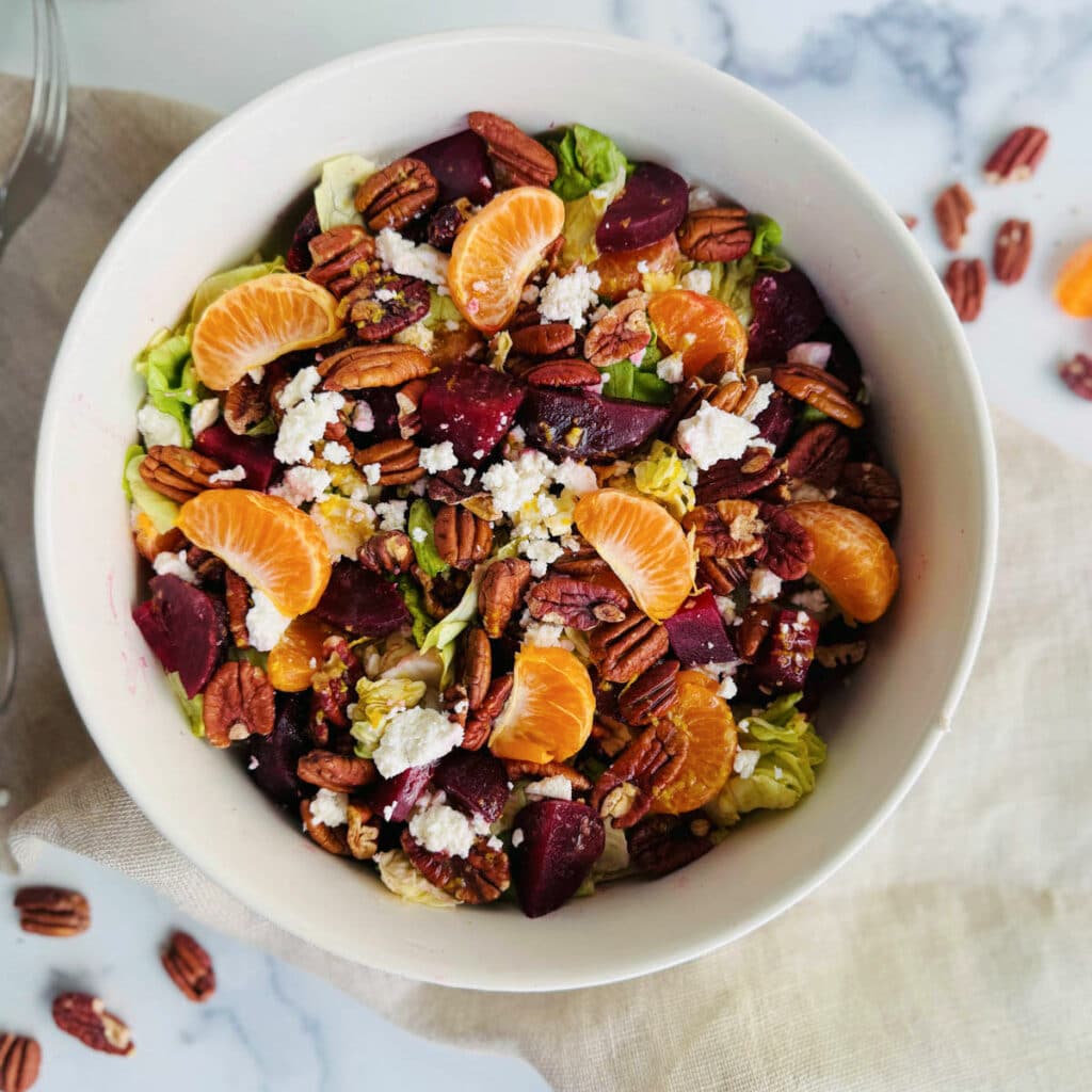 Beet, lettuce, orange sections, feta, and pecans with a homemade balsamic dressing in a white bowl.