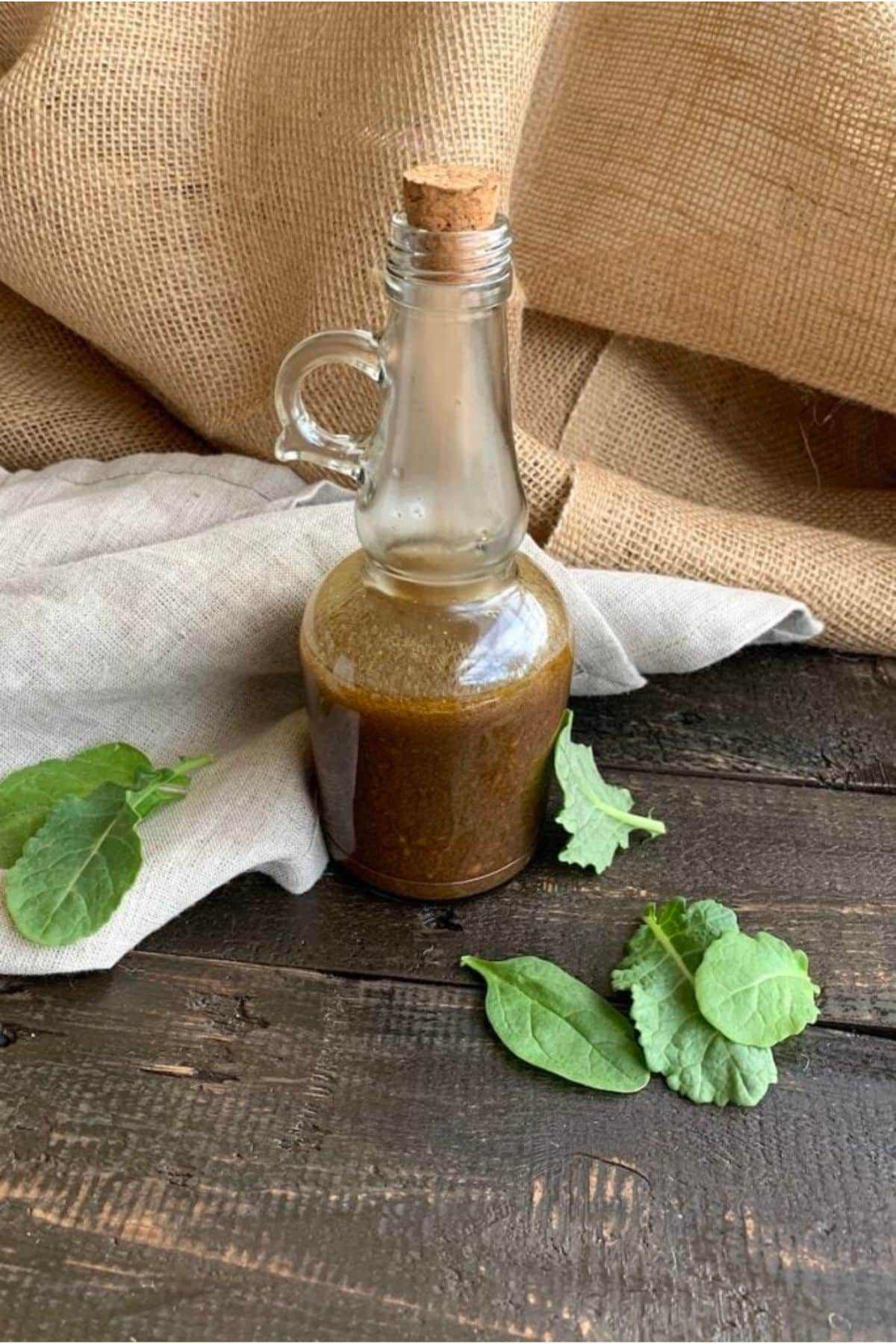 Bottle of salad dressing on black wooden table with basil and napkin.