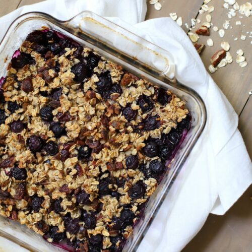 Baked oatmeal with blueberries in a glass dish on a white napkin.