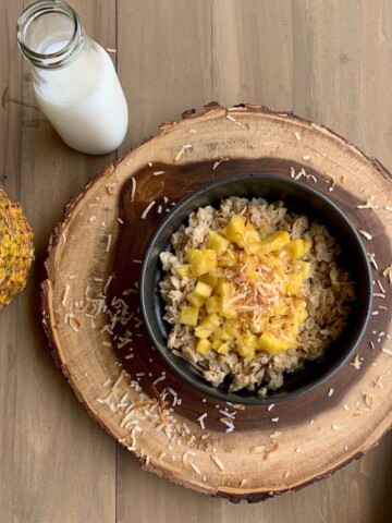 oatmeal porridge with pineapple and coconut in black bowl on wood slab