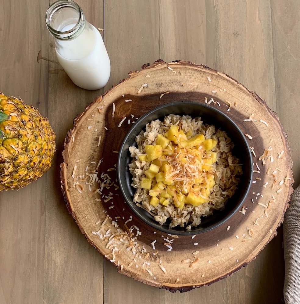 porridge with pineapple and coconut in black bowl on wood slab