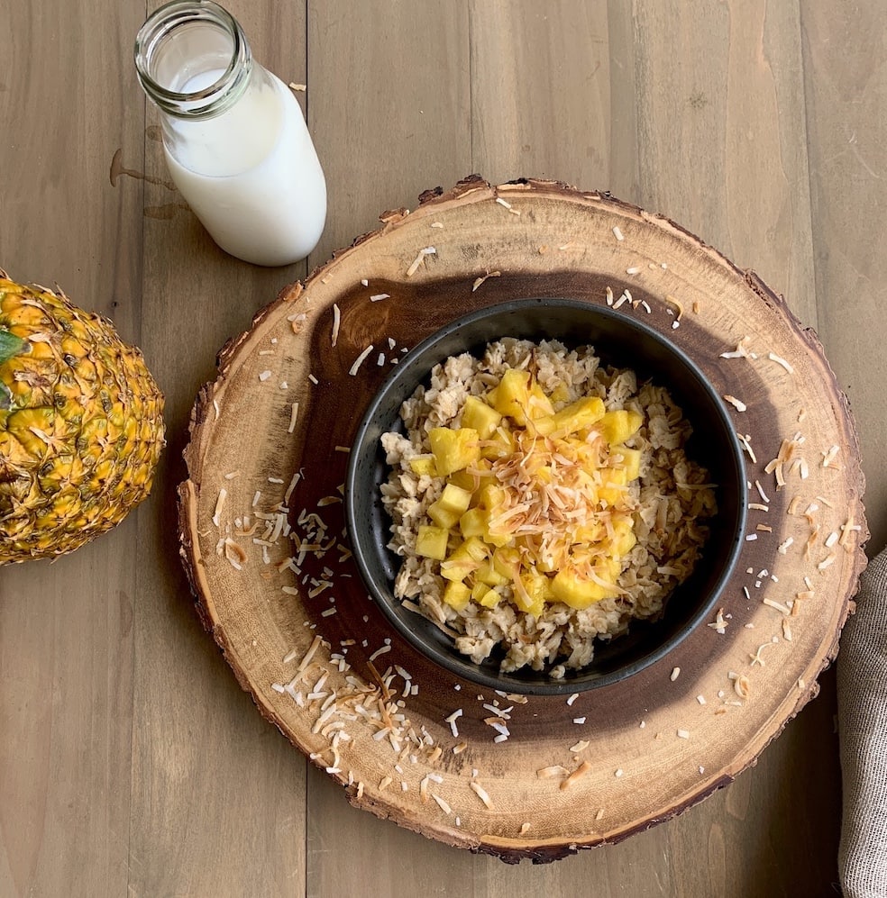 oatmeal porridge with pineapple and coconut in black bowl on wood slab