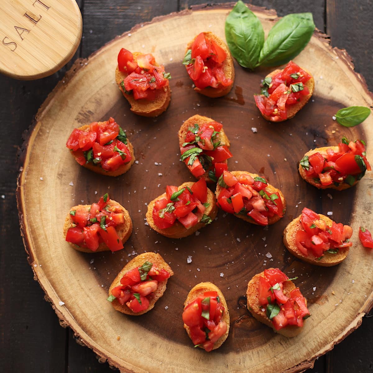 Tomatoes and basil on bread on a wood slab.