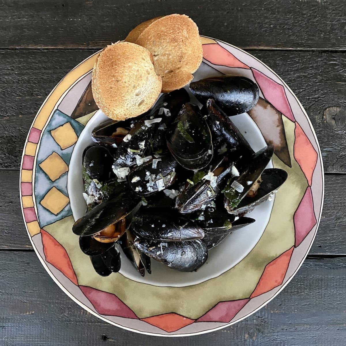 Mussels in serving bowl with slices of toasted bread on side.