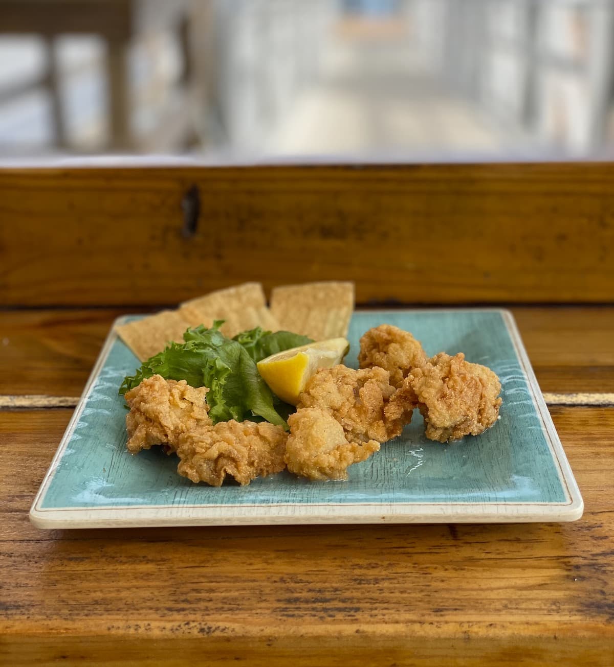Fried oysters on a blue plate on a wood bar.