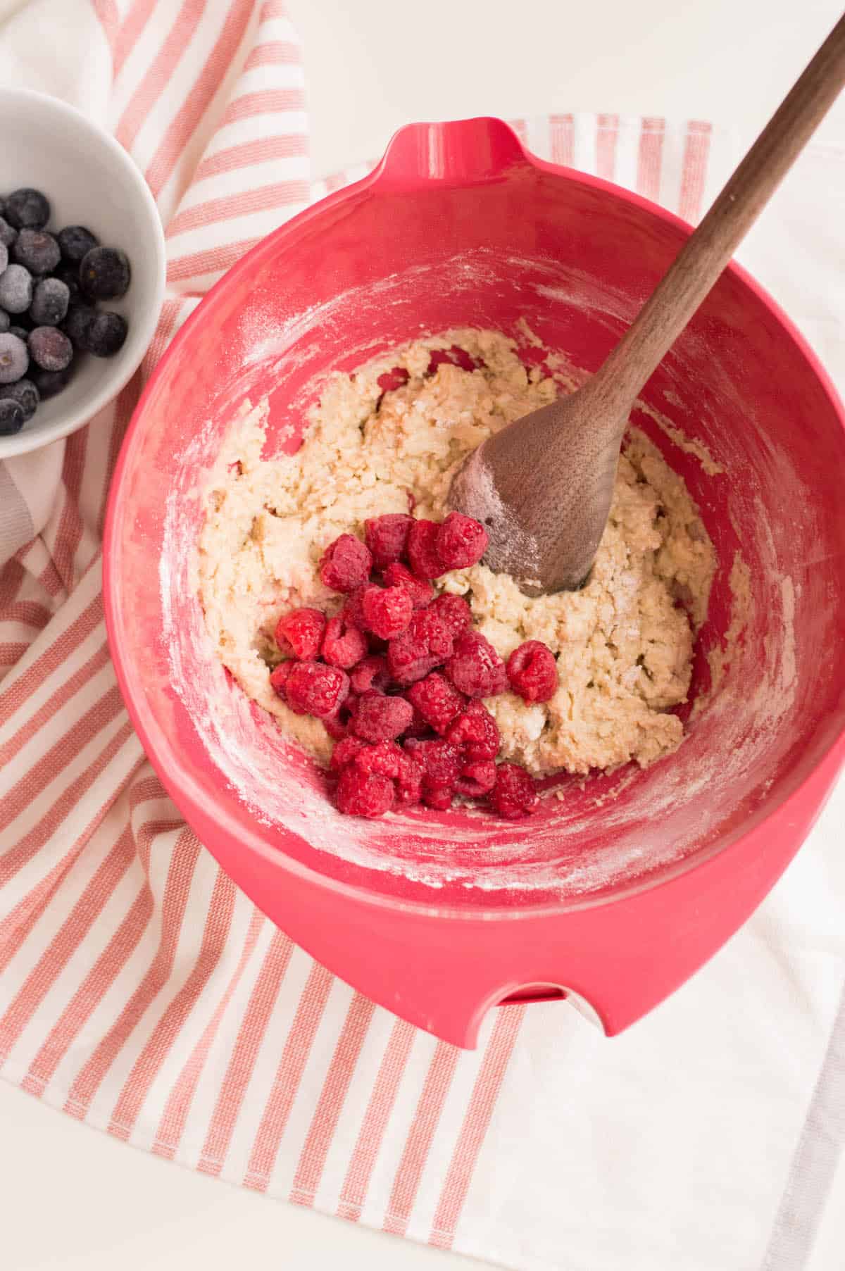 Berries in batter in red bowl on striped towel.