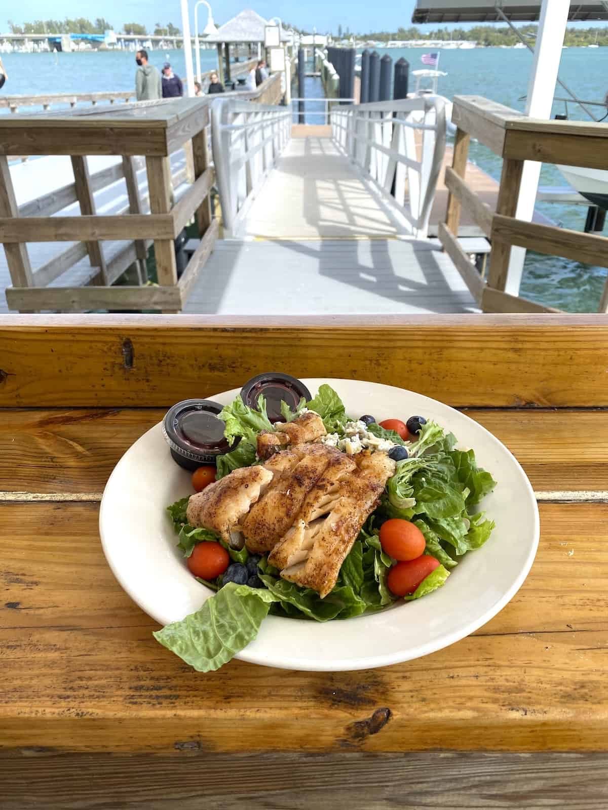 Grouper on a salad in a white bowl on a wood bar.