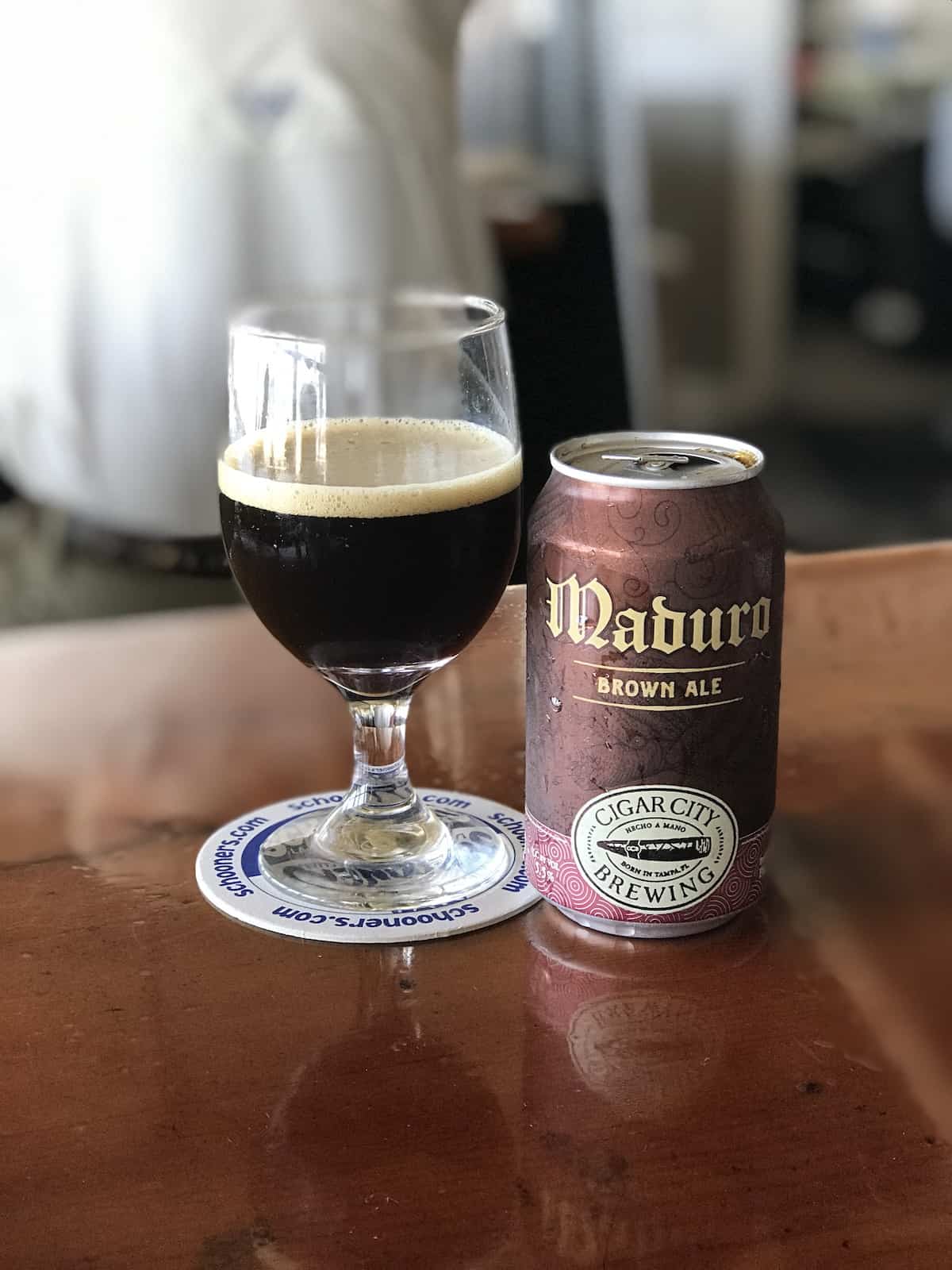 Local beer in glass with Maduro can next to it on a wood table.