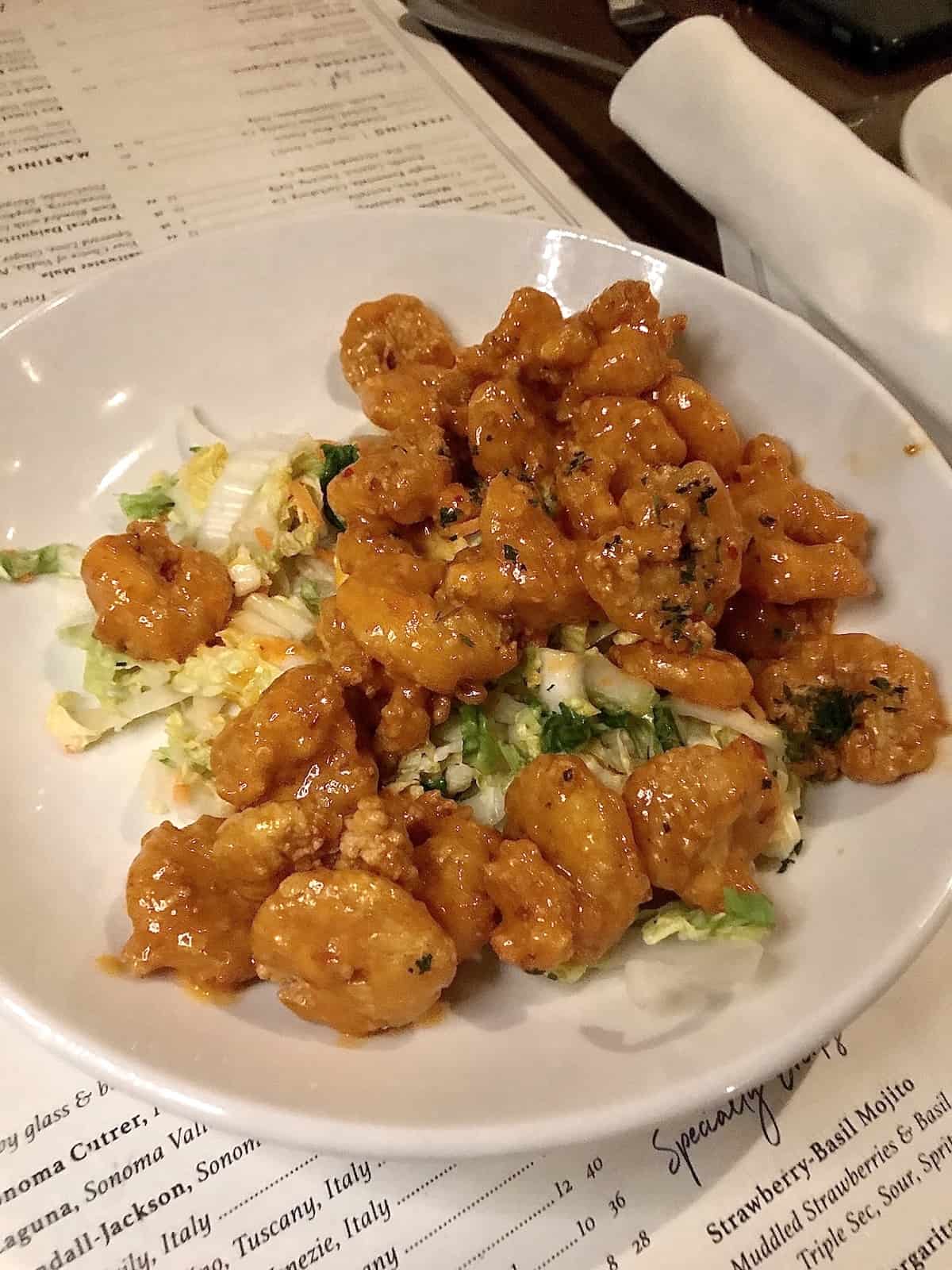 Fried shrimp with spicy sauce on lettuce on a white plate on a menu in a restaurant.