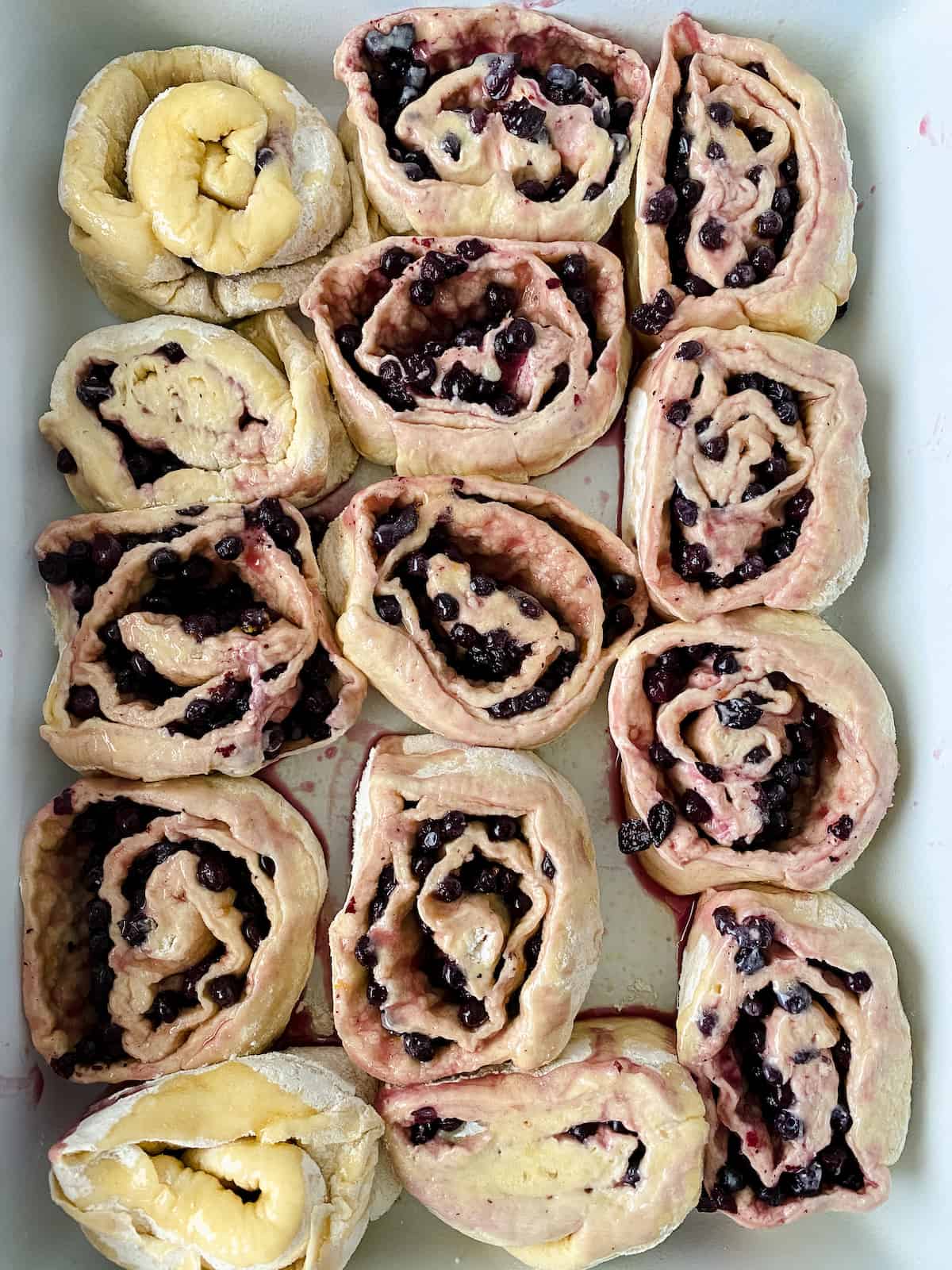 14 blueberry buns in a white baking dish before baking.