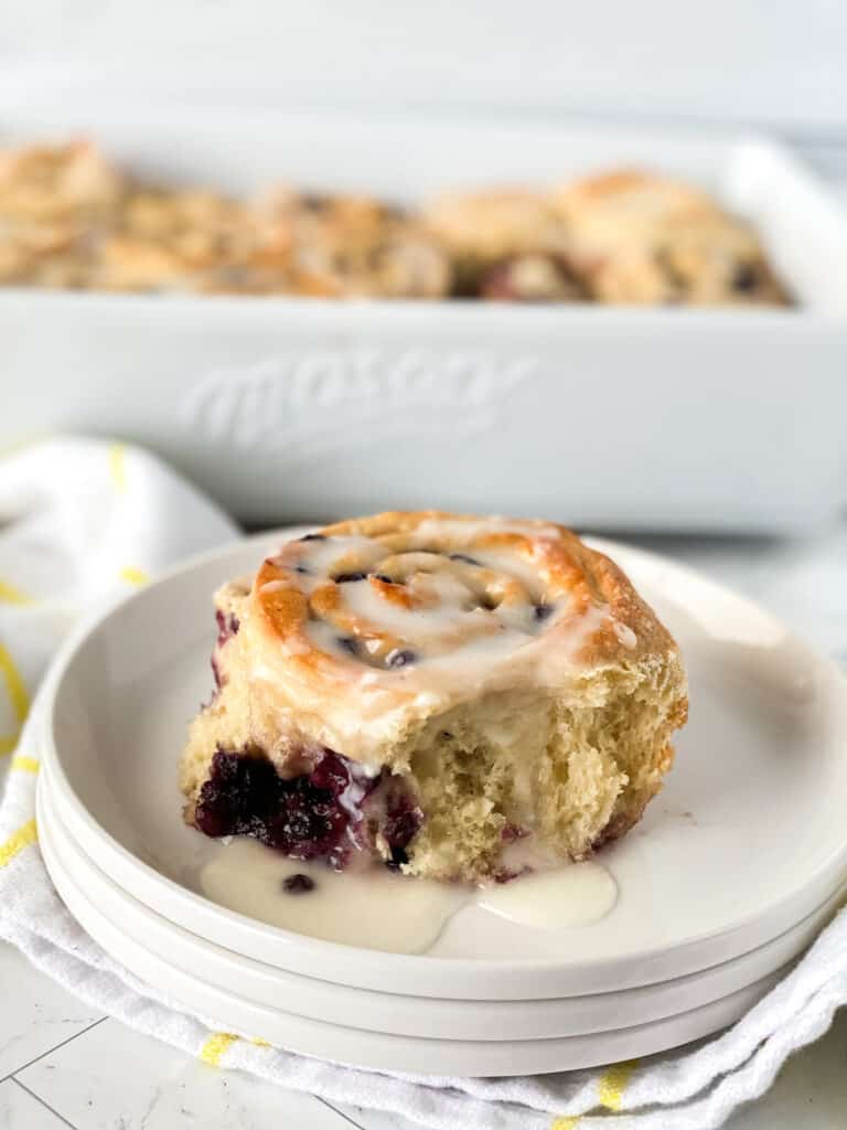 Blueberry sweet bun with icing on a white plate.