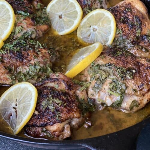 Chicken in a cast iron skillet with cilantro and lemons.