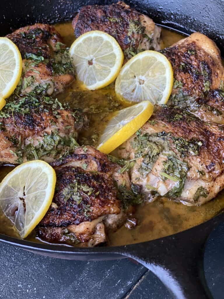 Chicken in a cast iron skillet with cilantro and lemons.