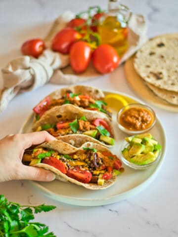Hand holding a quinoa taco with more tacos and ingredients in background.