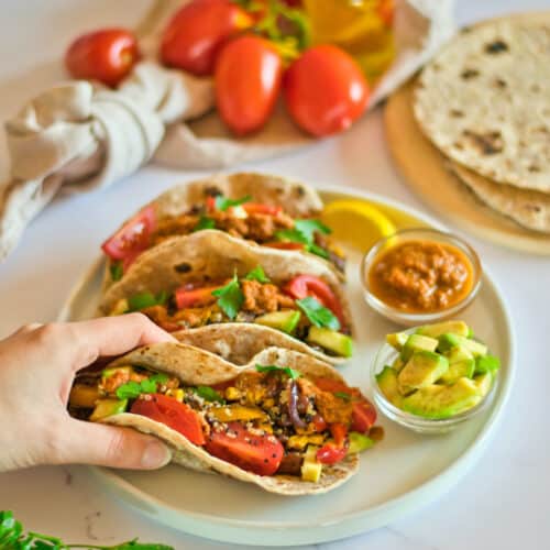 Hand holding a quinoa taco with more tacos and ingredients in background.