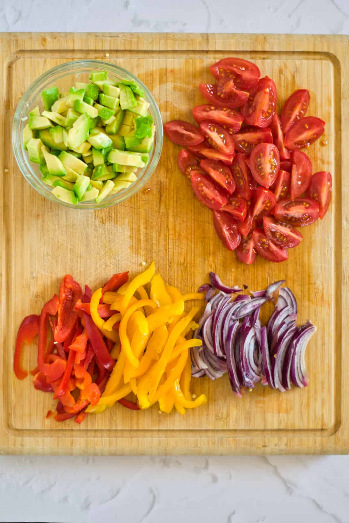 Peppers, onion, tomatoes, and avocado on a cutting board.