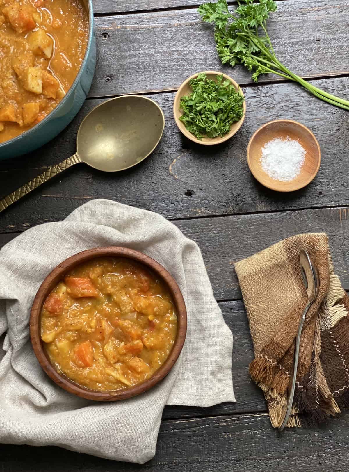 Roasted vegetable soup in a wood bowl on a black table with serving spoon.