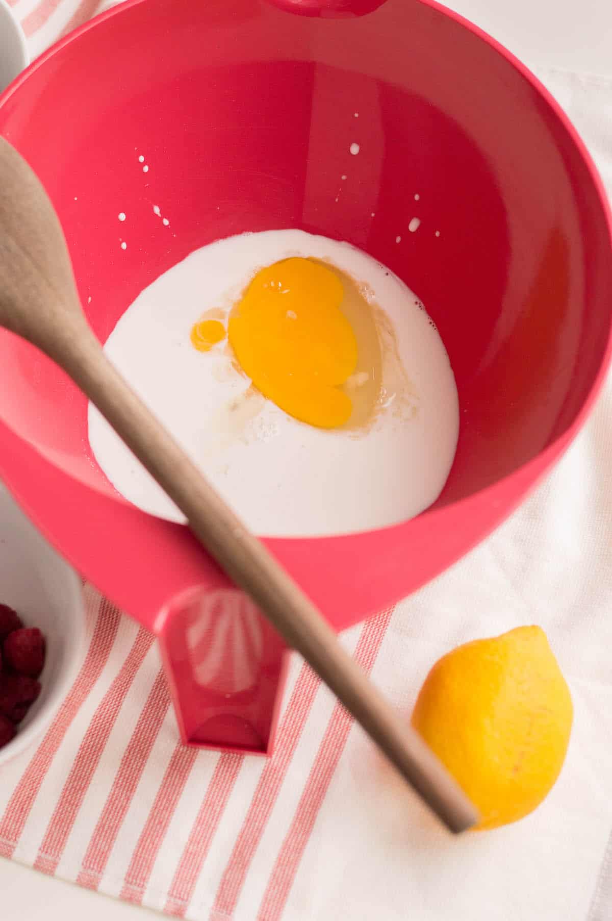 Egg and milk in red bowl on striped dishtowel.