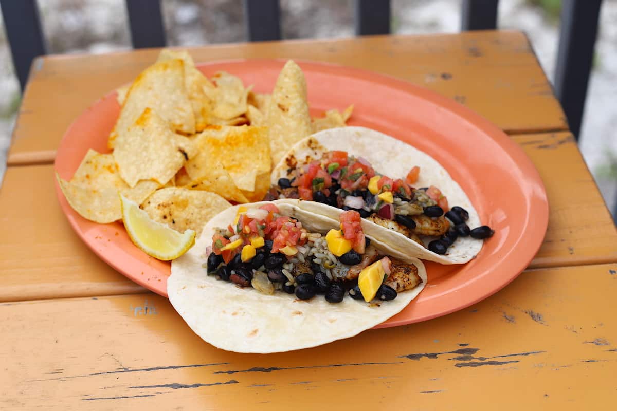 Tacos and chips on an orange plate on a orange wood table.