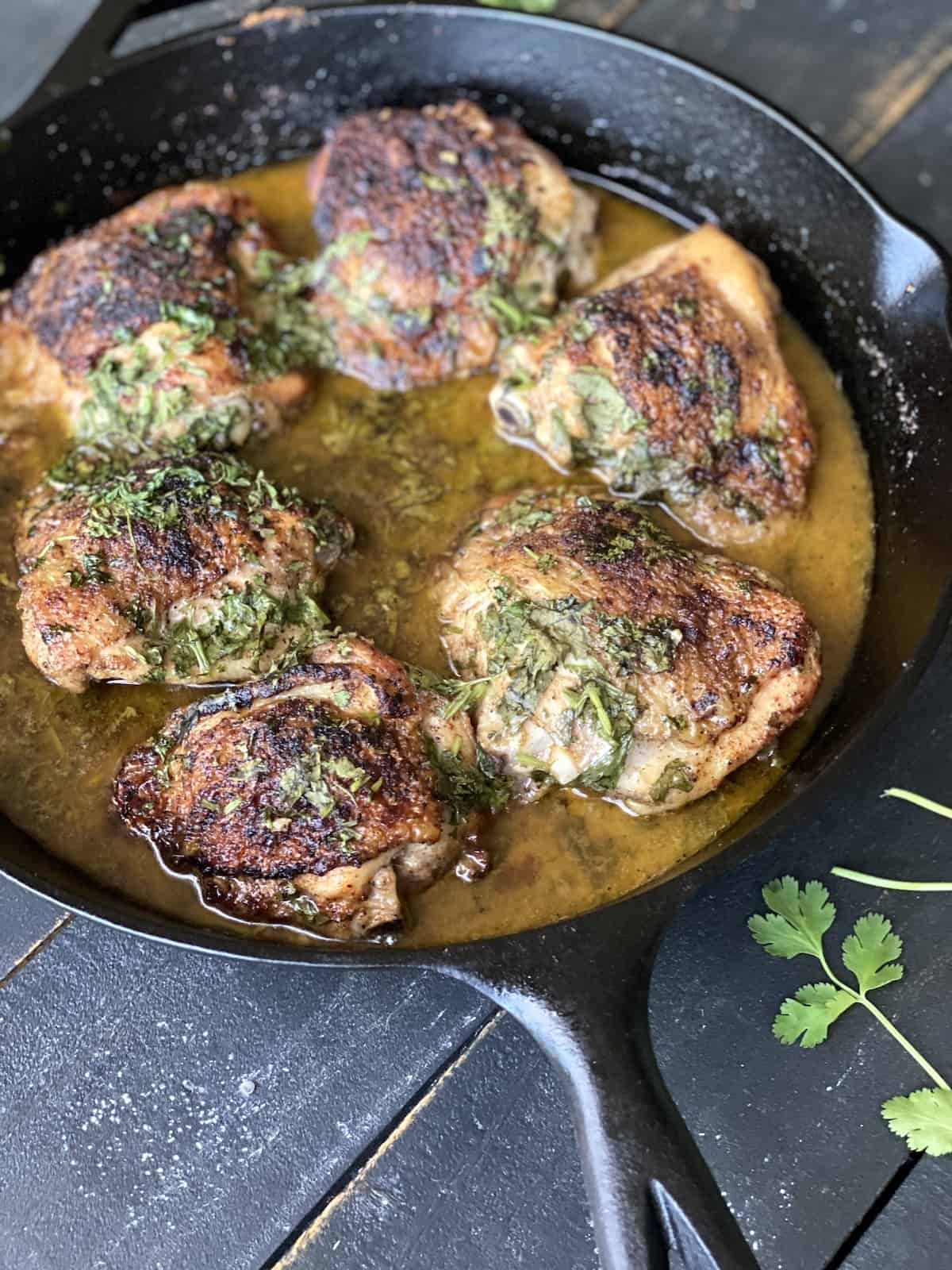 Chicken thighs cooked in a cast iron skillet on black table.