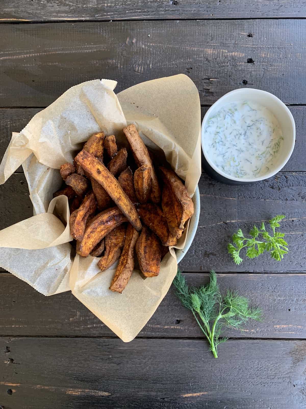 Sweet potato fries with dill dipping sauce on a black table.
