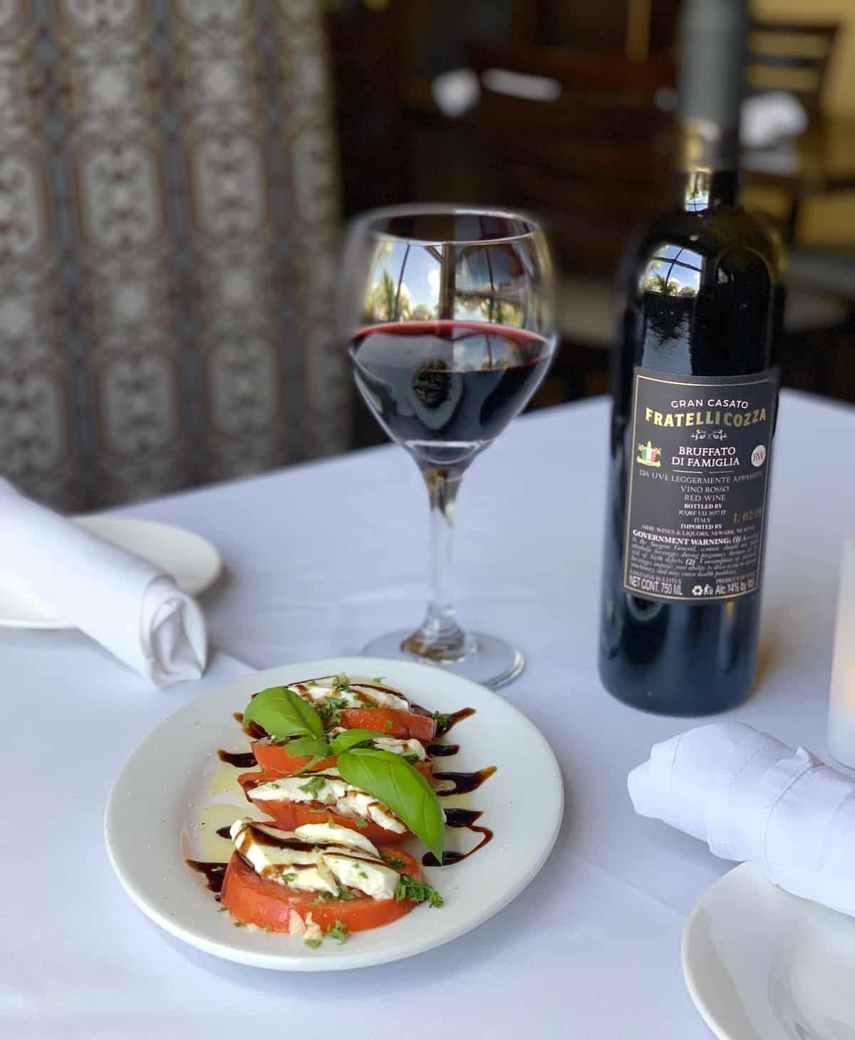 Tomato and mozzarella salad with a glass and bottle of wine in background.