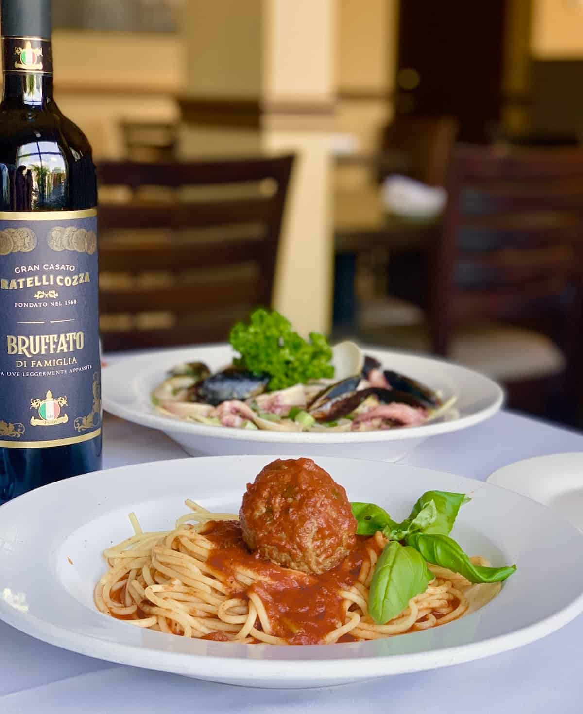 Spaghetti and meatballs, bottle of wine, seafood dish in background, all on white tabelcoth.