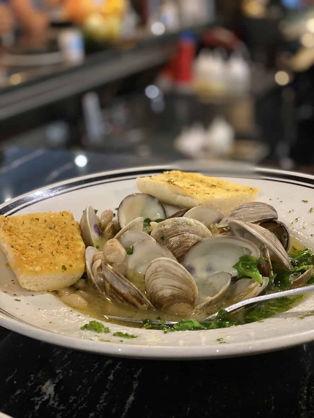 Clams, beans, and broccoli rabe in broth in a bowl with bread on side. 