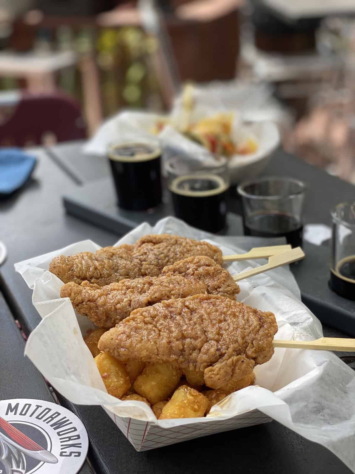 Fried chicken on a stick and tater tots with beer flight in background.